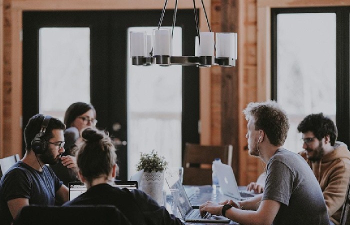 Several individuals are seated at a table with laptops, engaged in a discussion about streamlining sales through proposal automation software.